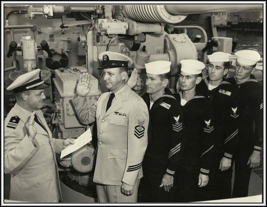 photograph of Captain Raymond E. Davis administering the Enlistment Oath to 5 unknown Savage shipmates. 