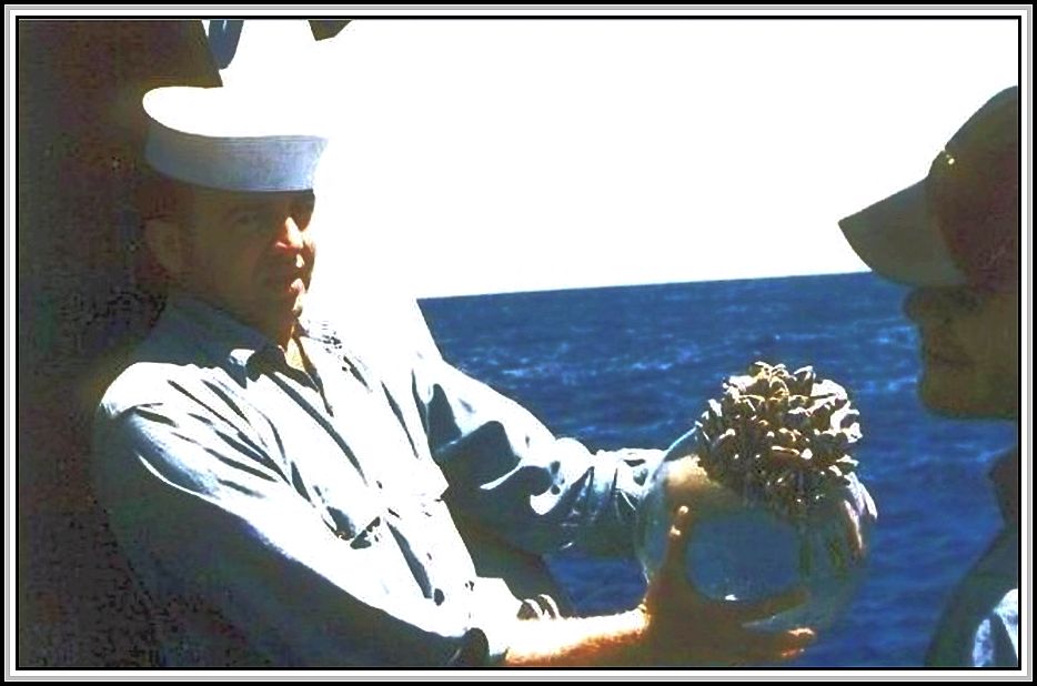 photograph of sailor holding fishing ball covered with barnacles